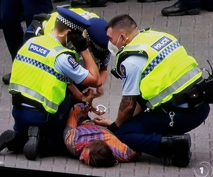 Police handcuff one of the three arrested men at the anti-mandate covid protest on Parliament grounds in Wellington