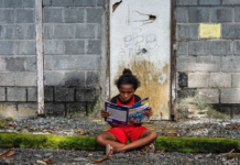 A Papuan girl reads a book in front of her house in Papua