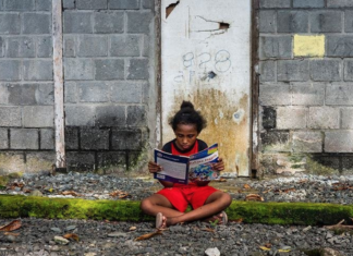 A Papuan girl reads a book in front of her house in Papua