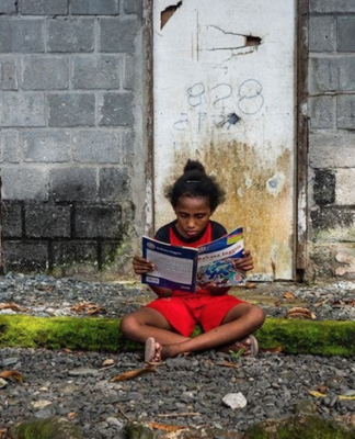 A Papuan girl reads a book in front of her house in Papua