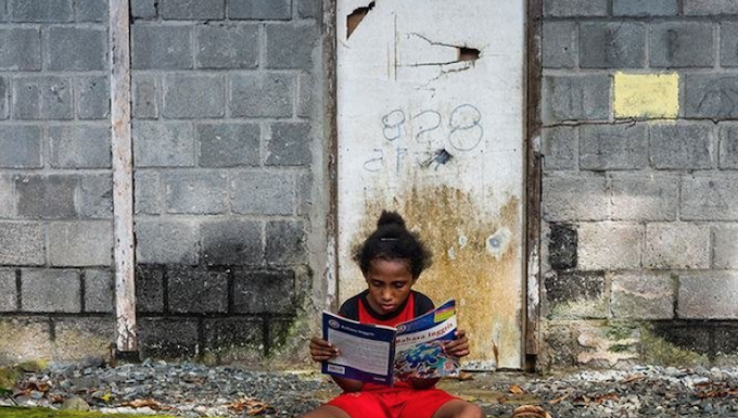 A Papuan girl reads a book in front of her house in Papua