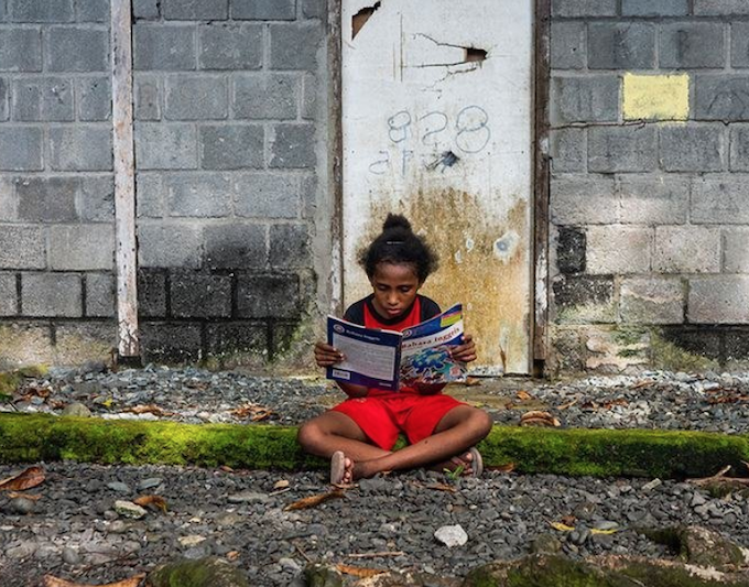 A Papuan girl reads a book in front of her house in Papua