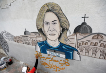A street artist adds to a mural of Al Jazeera reporter Shireen Abu Akleh