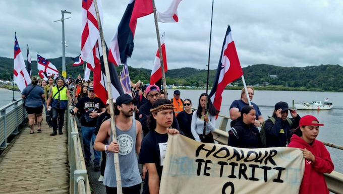 People holding a "Honour Te Tiriti o Waitangi" sign at Waitangi.