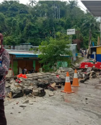 A woman in Jayapura stands next to a collapsed wall after the quake