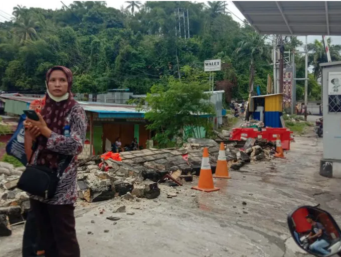 A woman in Jayapura stands next to a collapsed wall after the quake
