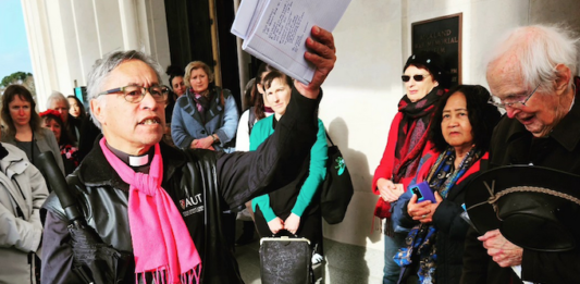 Activist minister Reverend Mua Strickson-Pua brandishes the petition against the AUKUS military pact at the launch