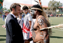 French President Emmanuel Macron shakes hands with a traditional Kanak dancer