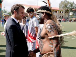 French President Emmanuel Macron shakes hands with a traditional Kanak dancer