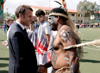French President Emmanuel Macron shakes hands with a traditional Kanak dancer