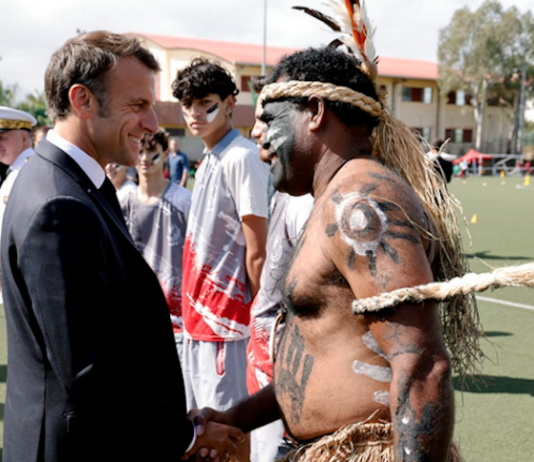 French President Emmanuel Macron shakes hands with a traditional Kanak dancer