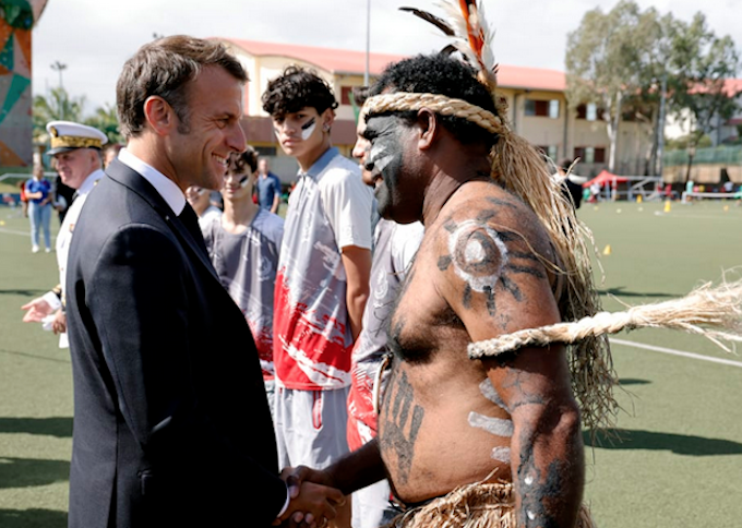 French President Emmanuel Macron shakes hands with a traditional Kanak dancer