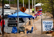 The flag of Hawai'i waves beside a sign reading "Tourist(s) Keep Out" in the aftermath of the Maui wildfires