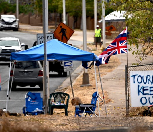 The flag of Hawai'i waves beside a sign reading "Tourist(s) Keep Out" in the aftermath of the Maui wildfires