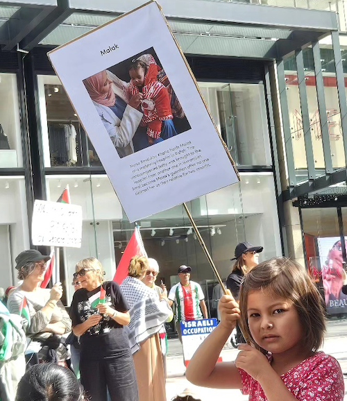 A young girl at the Auckland rally holds a placard in a tribute for a Gazan nurse