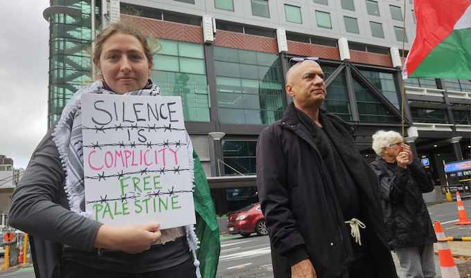 A protester holds a "Silence is complicity" placard outside TVNZ