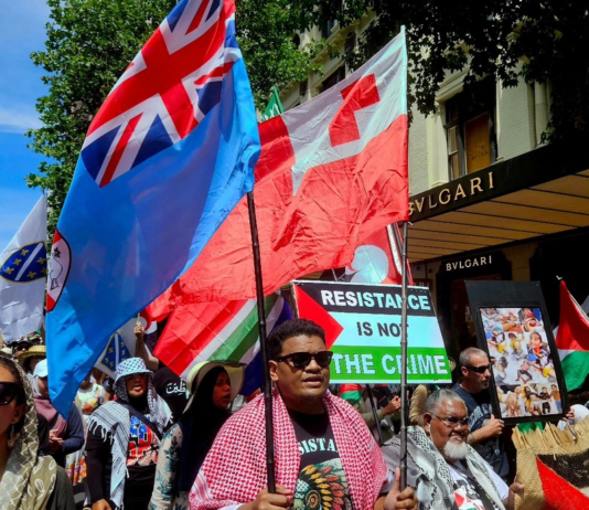 Pacific flags -- Fiji and Tonga -- and protesters in support of Palestine at a rally in New Zealand's largest city Auckland