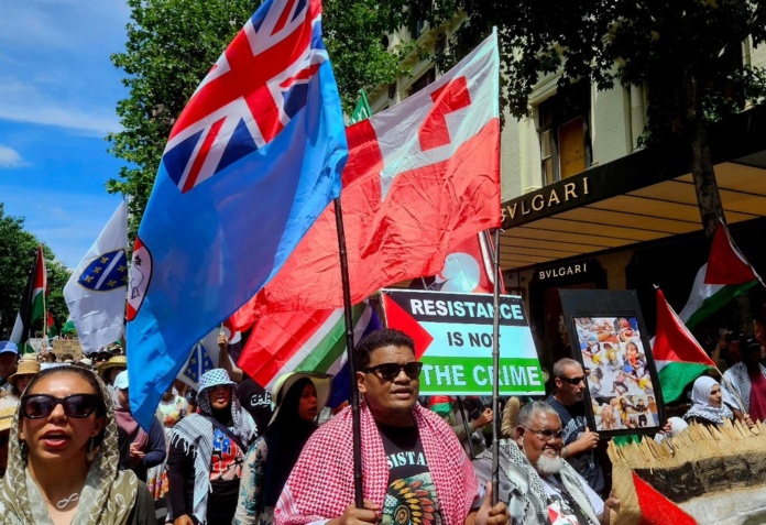 Pacific flags -- Fiji and Tonga -- and protesters in support of Palestine at a rally in New Zealand's largest city Auckland