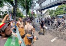 Security forces watch from behind barbed wire as indigenous Papuans from Merauke in the Indonesia-ruled Melanesian region protest