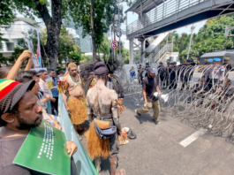 Security forces watch from behind barbed wire as indigenous Papuans from Merauke in the Indonesia-ruled Melanesian region protest