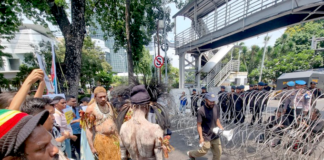 Security forces watch from behind barbed wire as indigenous Papuans from Merauke in the Indonesia-ruled Melanesian region protest