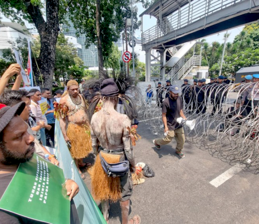 Security forces watch from behind barbed wire as indigenous Papuans from Merauke in the Indonesia-ruled Melanesian region protest