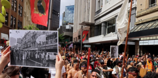 John Miller's photograph of the 1975 Land March held up in the same location at the 2024 Hīkoi mō te Tiriti in Pōneke Wellington.