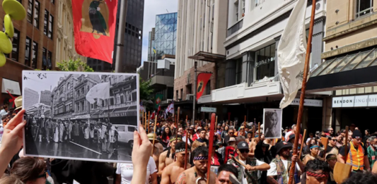 John Miller's photograph of the 1975 Land March held up in the same location at the 2024 Hīkoi mō te Tiriti in Pōneke Wellington.