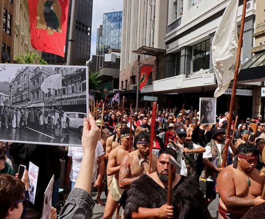 John Miller's photograph of the 1975 Land March held up in the same location at the 2024 Hīkoi mō te Tiriti in Pōneke Wellington.