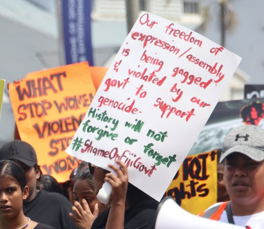 An "Our freedom of expression/assembly is being gagged and violated by our government to support genocide" placard