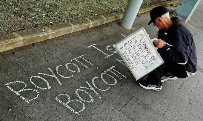 A protester chalks a "Boycott Israel, boycott genocide" sign on the pavement near Auckland Hospital today