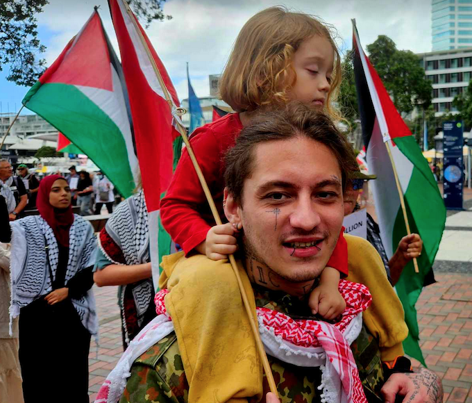 A father piggybacks his sleepy child during the New Zealand solidarity protest for Palestine in Auckland's Viaduct 