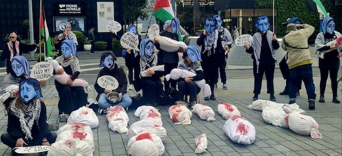 Starvation masks, banners, placards and mock bodies make a dramatic street theatre scene in Auckland's Takutai Square