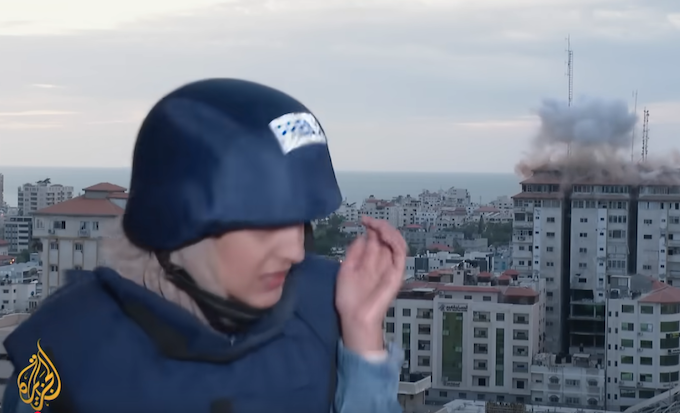 An Al Jazeera reporter ducks for cover as bombs hit a building behind her