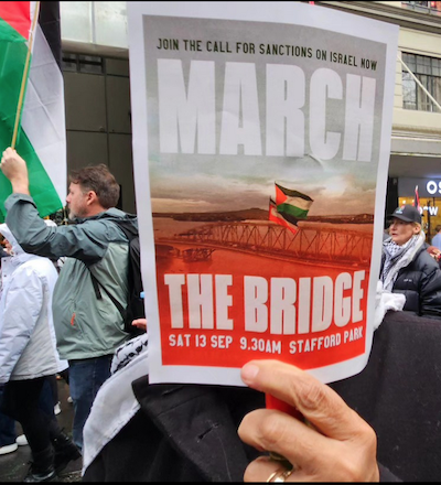A protester holds up a "March The Bridge" flyer for Gaza