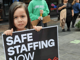 A child holds a medical "safe staffing" placard at the mega strike in Auckland