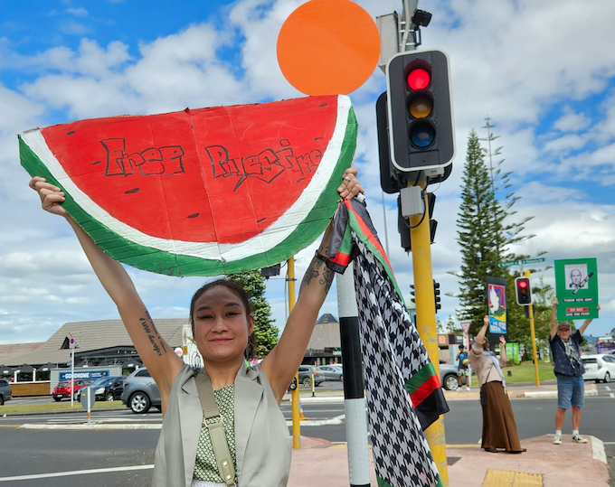 A New Zealand pro-Palestine protester with a watermelon "Free Palestine" placard at traffic lights in a West Auckland rally