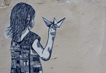 Street art depicting a girl holding a paper boat, with half of her dress showing buildings