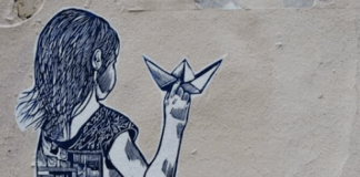 Street art depicting a girl holding a paper boat, with half of her dress showing buildings