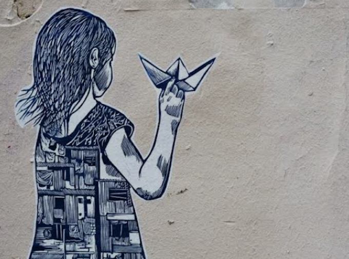 Street art depicting a girl holding a paper boat, with half of her dress showing buildings