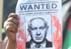 A woman protester holds up a “Wanted” poster featuring Israel’s Prime Minister Benjamin Netanyahu