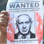 A woman protester holds up a “Wanted” poster featuring Israel’s Prime Minister Benjamin Netanyahu