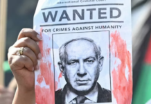 A woman protester holds up a “Wanted” poster featuring Israel’s Prime Minister Benjamin Netanyahu