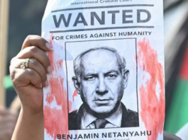 A woman protester holds up a “Wanted” poster featuring Israel’s Prime Minister Benjamin Netanyahu