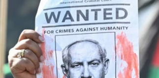 A woman protester holds up a “Wanted” poster featuring Israel’s Prime Minister Benjamin Netanyahu