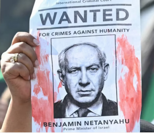A woman protester holds up a “Wanted” poster featuring Israel’s Prime Minister Benjamin Netanyahu