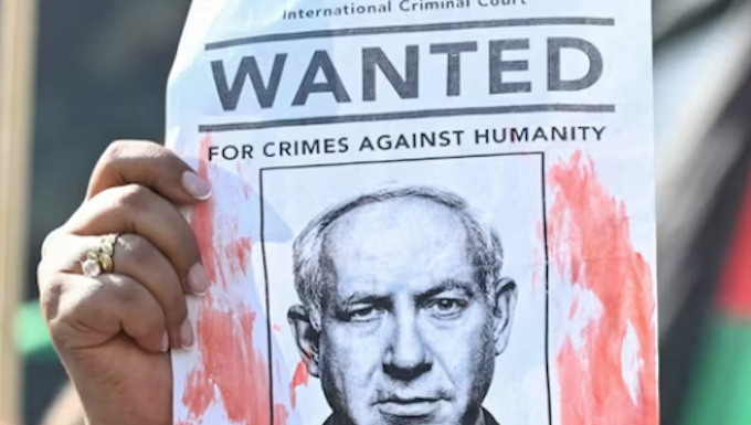 A woman protester holds up a “Wanted” poster featuring Israel’s Prime Minister Benjamin Netanyahu