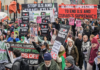 Protesters wave flags and banners reading “Stop Bombing Iran” and “Stop Bombing the Middle East” as they gather at Victoria Tower Gardens in London
