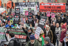 Protesters wave flags and banners reading “Stop Bombing Iran” and “Stop Bombing the Middle East” as they gather at Victoria Tower Gardens in London