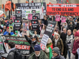 Protesters wave flags and banners reading “Stop Bombing Iran” and “Stop Bombing the Middle East” as they gather at Victoria Tower Gardens in London